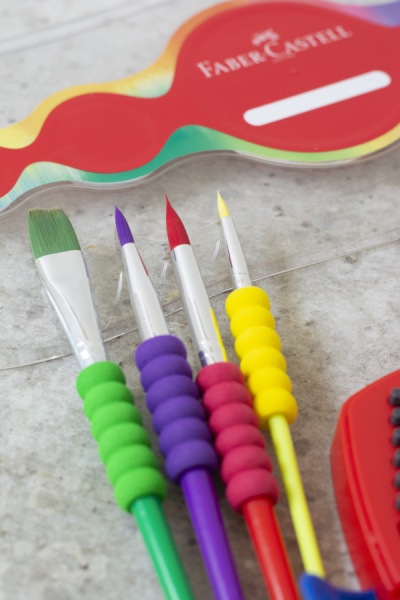 Farbige Pinsel mit ergonomischen Griffen und ein Aquarellkasten von Faber-Castell.