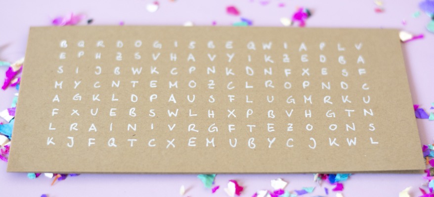 Karte mit großem Buchstabenrätsel auf braunem Papier mit Konfetti