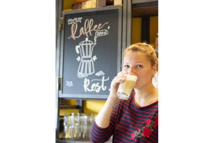 Frau trinkt Kaffee vor Tafel mit Kreidezeichnung eines Espressokochers