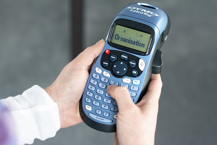 Person tippt „Organisation“ auf einem Dymo-Beschriftungsgerät ein.