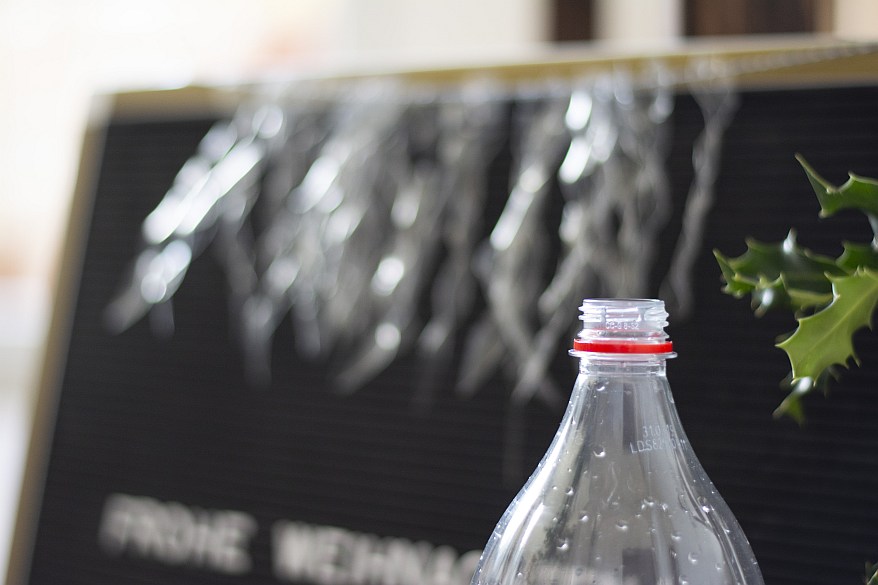 Leere Plastikflasche vor DIY-Eiszapfen aus recyceltem Plastik an einer Tafel.