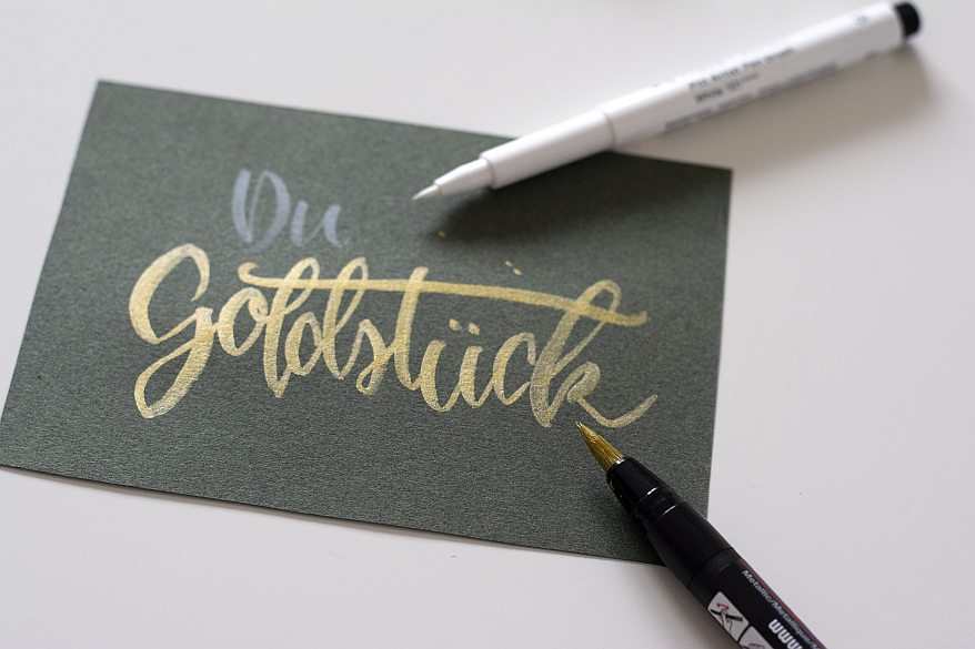 Handlettering „Du Goldstück“ in Gold auf dunkler Karte mit Brushpen und Marker von Faber-Castell