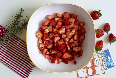 Kleingeschnittene Erdbeeren in Schüssel, daneben Etiketten und Rosmarin.