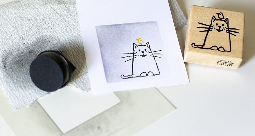  Eine gestempelte Katze auf Papier, daneben liegt ein Holzstempel.