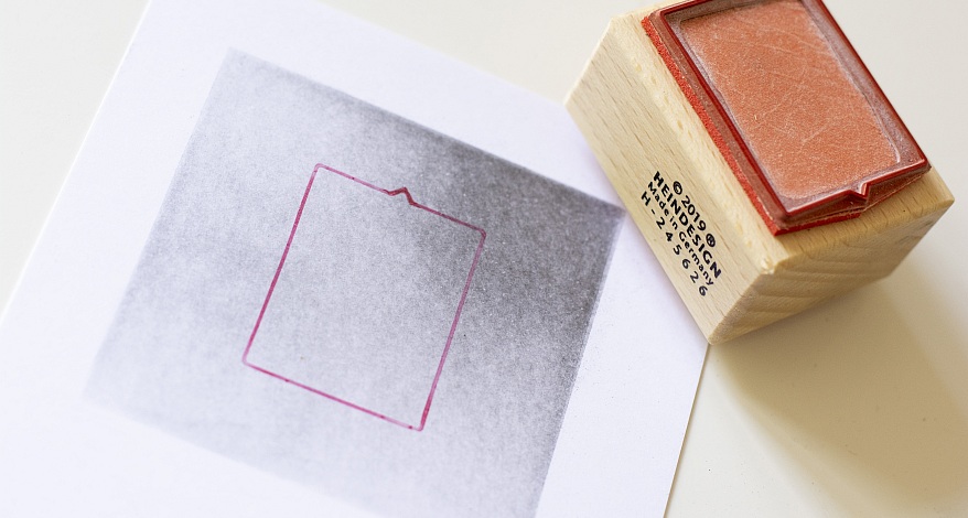 Gestempelter Rahmen auf schattiertem Hintergrund, der mit Hilfe der Radiertechnik gemacht wurde. Daneben ein Holzstempel.