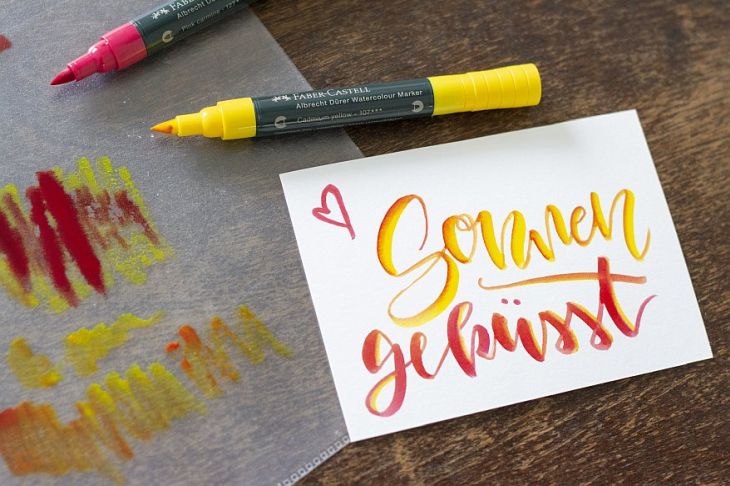 Klarsichtfolie, gelber und roter Stift und eine mit gelb und rot beletterte Karte mit Text "Sonnengeküsst" auf einem Tisch