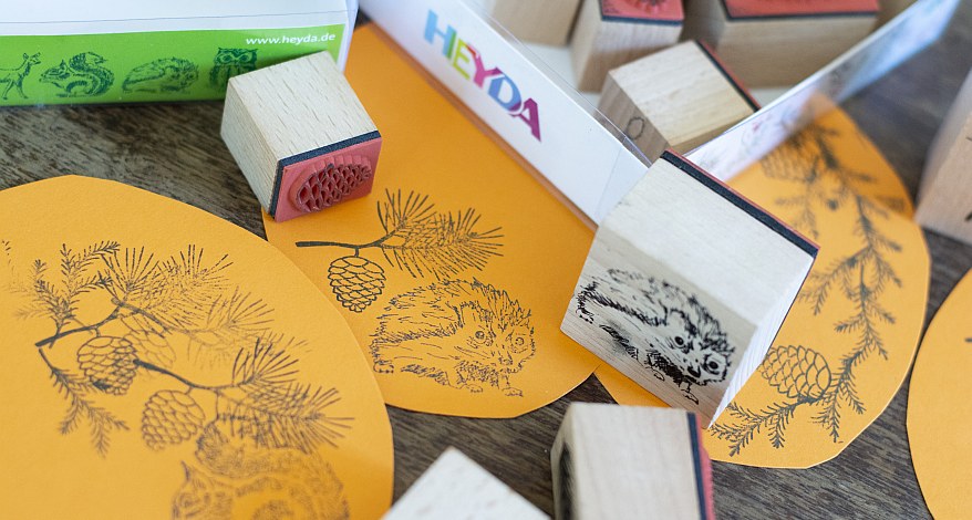 Teile der Papierkürbis sind mit Stempeln in herbstlichen Motiven wie Igel, Tannenzweige dekoriert. Die Stepel der Marke Heyda liegen auf den Schablonen.