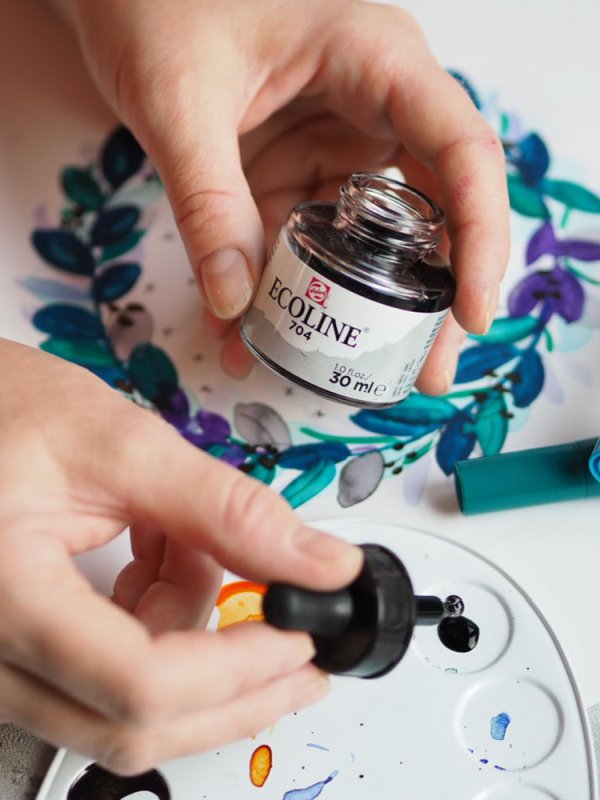 Hände öffnen eine Flasche Ecoline-Aquarellfarbe über einer Malpalette