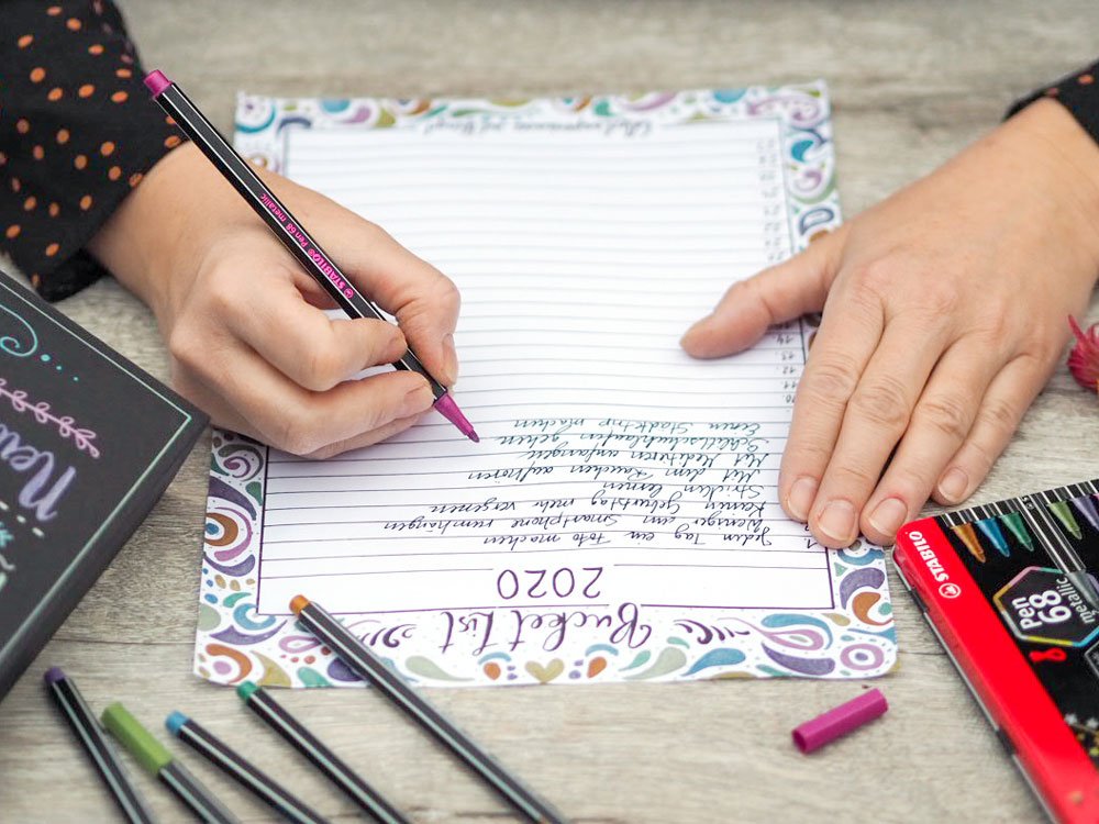 Eine Person füllt eine Bucket List für das Jahr 2020 aus. Sie benutzt dafür die Metallic Marker von Stabilo. Im Vordergrund liegen weitere Stifte von Stabilo sowie eine Metallbox.