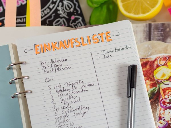 Handgeschriebene Einkaufsliste im Meal-Prep-Ordner mit Zitrone