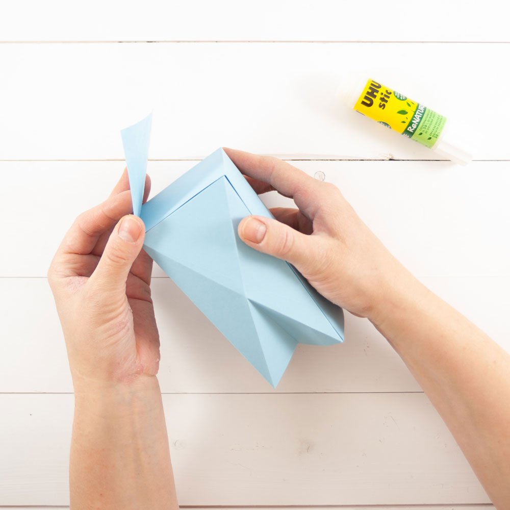 Zwei Hände kleben eine ausgeschnittene Schachtel zusammen.