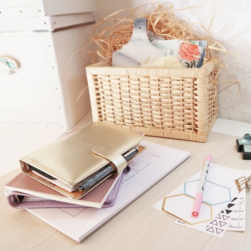 Auf einem Tisch liegen Notizblöcke, 2 Filofax-Kalender, Sticker und ein Stift. Außerdem steht ein Korb mit diversen Bastelmaterialien daneben.