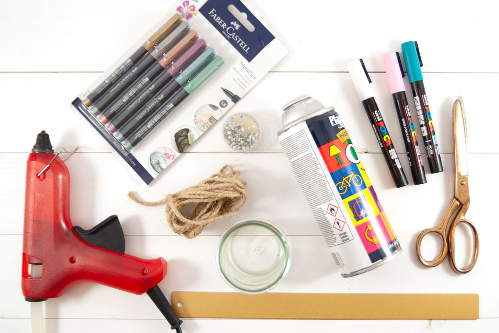 Heißklebepistole, Scheren, Glas, bunte Stifte und Spraydose liegen auf einem Tisch