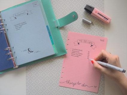 Hand schreibt To-do-Liste auf rosa Seite mit Marker, daneben offener Planner.