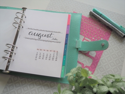 Aufgeschlagener Planer zeigt August-Kalenderblatt, daneben Deko.