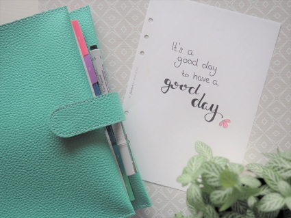 Türkiser Planner, daneben Blatt mit gelettertem Text "It's a good day to have a good day"