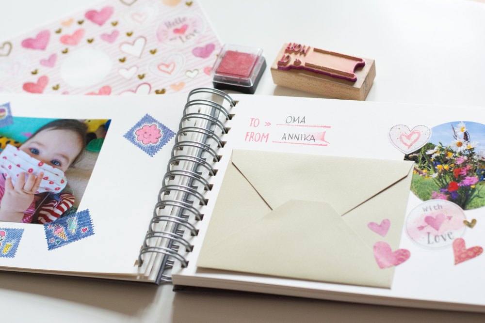IOn dem aufgekallpten Ringbuch von Semikolon ist ein Babyfoto mit Stickern rundherum auf der linken Seite eingeklebt. Auf der rechten Seite ist ein kleiner Briefumschlag, Sticker in Herzform und ein Foto ,it einem Blumenstrauß eingeklebt.