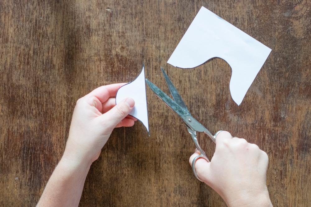 Eine Hand hält eine Schablone fest, die ander schneidet sie mit einer Schere aus.
