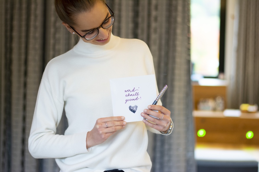 Eine junge Frau hält eine gestaltete Gute Bersserungs Karte in der Hand und schaut lächelnd darauf.