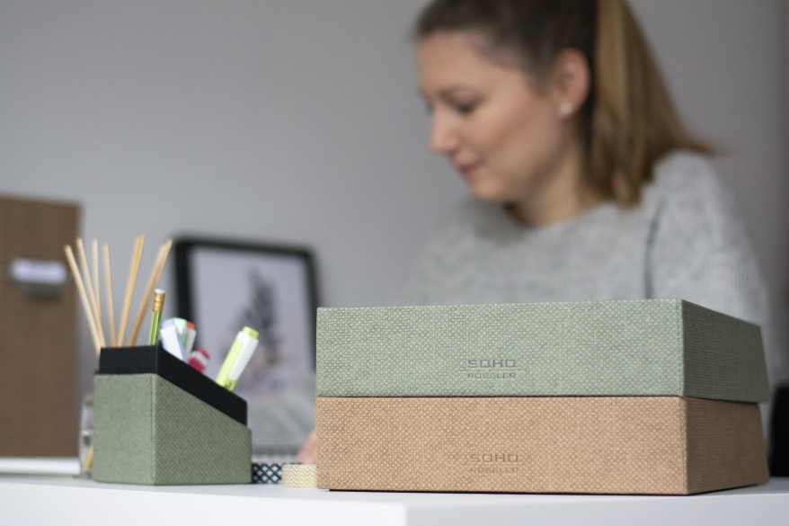 Frau sitzt im Homeoffice am Schreibtisch. Im Vordergrund sieht man einen Stifteköcher und Ablageschalen der S.O.H.O.-Serie von Rössler.