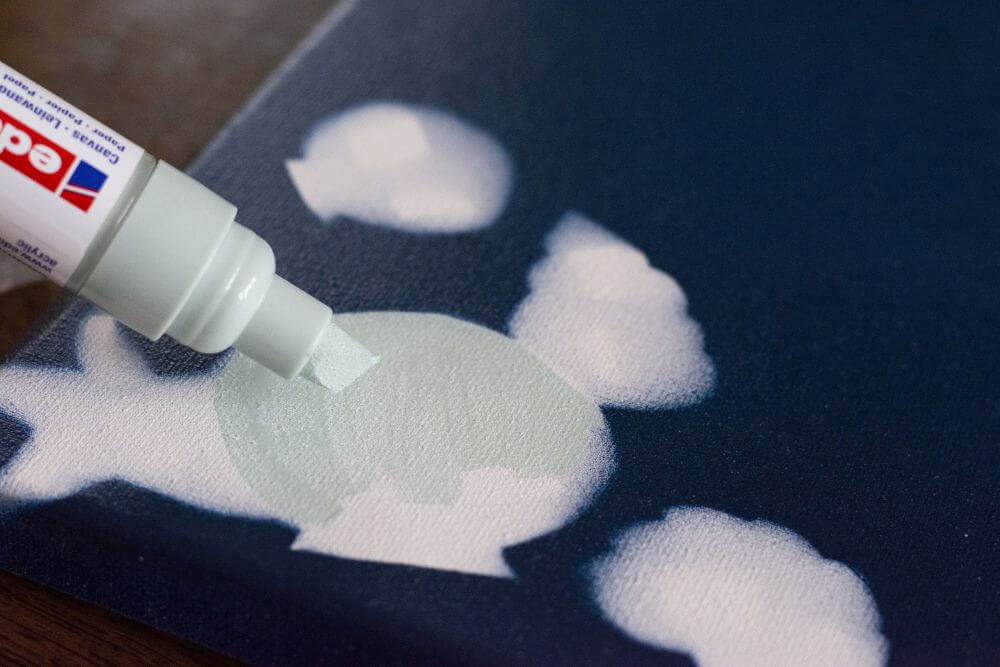 Nahaufnahme eines Acrylmarkers mit Keilspitze von Edding, der eine Muschel auf Leinwand malt.