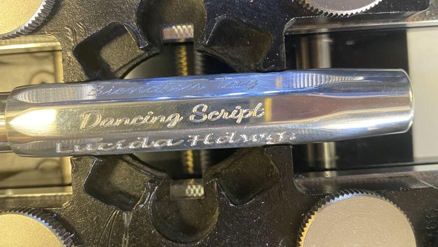 Nahaufnahme eines Schreibgeräts in einer Graviermaschine, auf dem unterschiedlichen Schriftarten zu sehen sind.