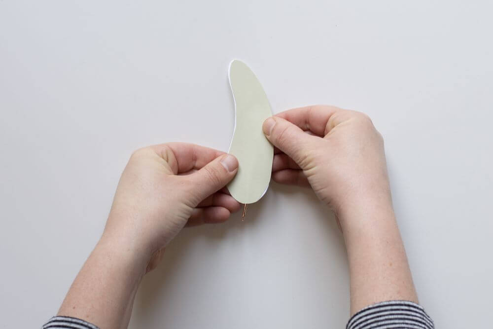 Bastelanleitung Do it yourself-Papierfedern. Schritt 5: Papierausschnitt auf die Rückseite des selbstklebenden Motivkartons aufkleben.