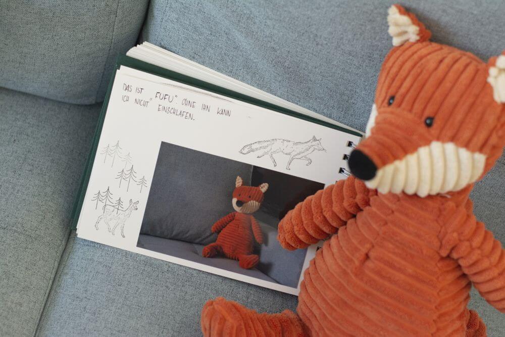 Ein Trostalbum für Kindergartenkinder liegt auf einem Sofa. Abgebildet auf einem Foto ist der Fuchs als Lieblingskuscheltier, der in echt daneben sitzt.