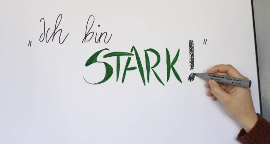 Eine Hand schreibt mit dem Flipchartmarker Lumocolor von Staedtler "Ich bin stark!" auf ein Papier.
