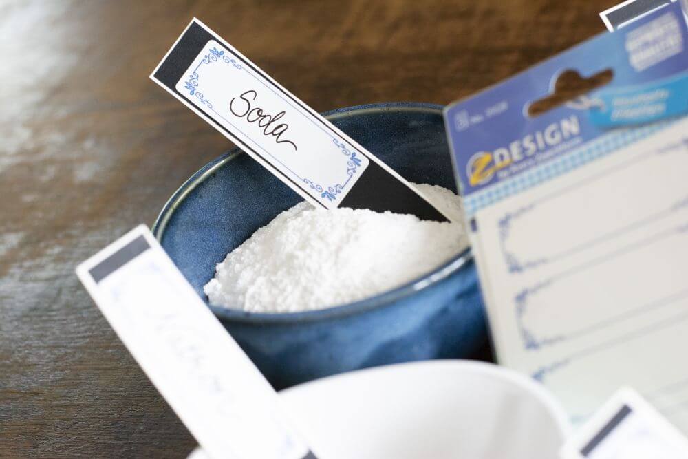 Zutaten für DIY-Haushaltsmittel (Soda, Natron, Kernseife) sind in Schalen auf einem Küchentisch aufgestellt. Daneben liegt ein Stickerbogen von Avery Zweckform.