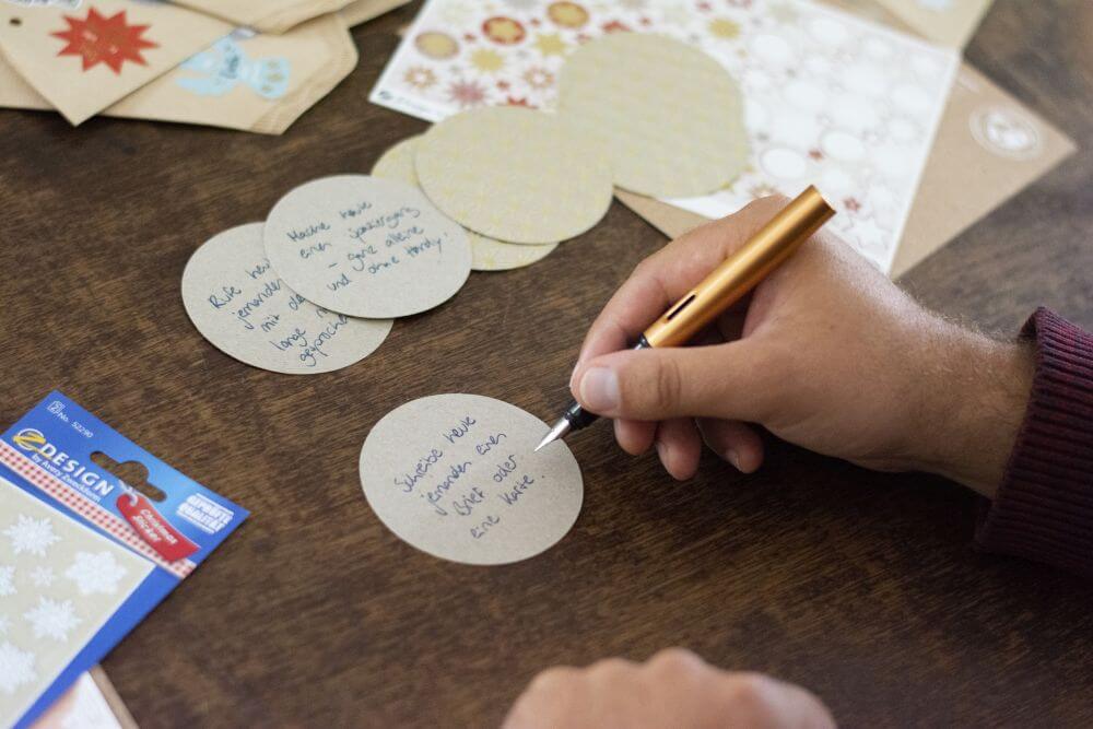 Eine Hand beschriftet mit einem goldenen Füller einen Motivkarton in Kreisform. Daneben liegen Sticker von Avery Zweckform.
