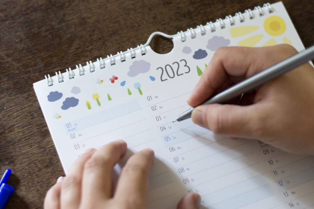 Eine Hand schreibt in einen Familienplaner von Heye in die Jahresübersicht 2023.