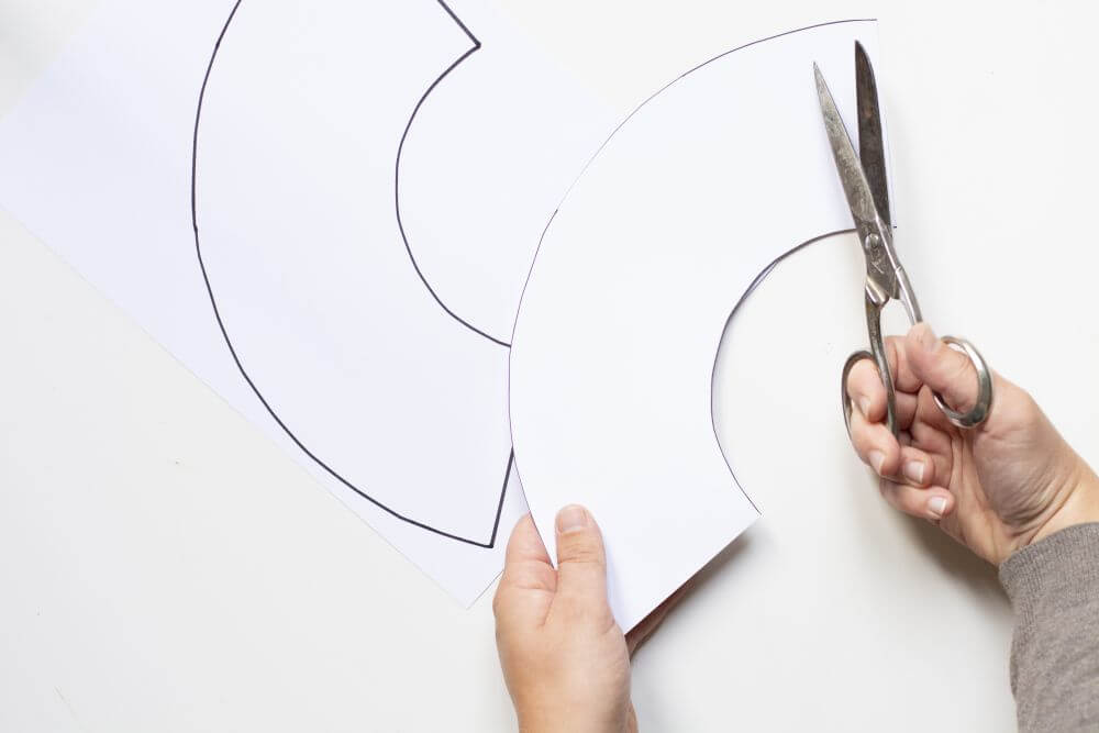 Eine Person schneidet Halbkreise aus einem weißen Papier. 