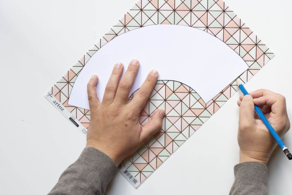 Eine Person legt einen weißen Halbkreis auf buntes Papier und umrandet den Halbkreis.