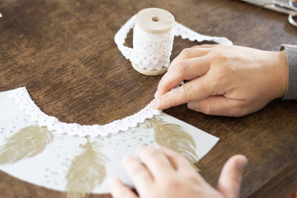 Eine Person klebt Spitzenbänder auf einen weißen Papier-Halbkreis.