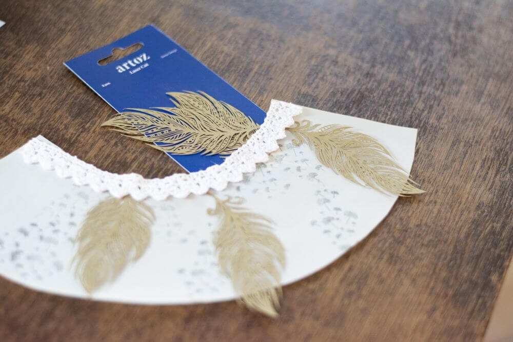 Ein halbkreisförmiges weißes Transparentpapier mit grauen Federn auf einem Holztisch.