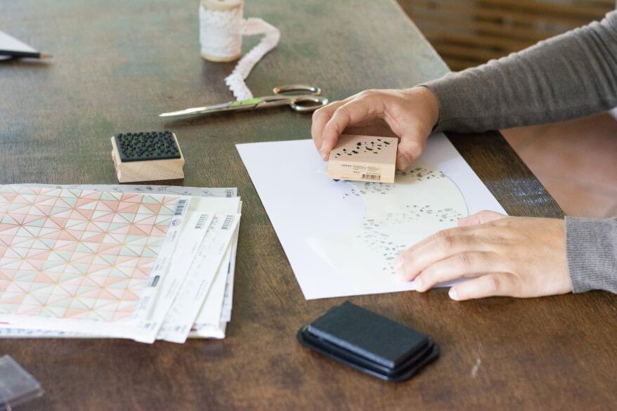 Person bestempelt Papier für eine DIY-Bastelarbeit auf einem Holztisch.