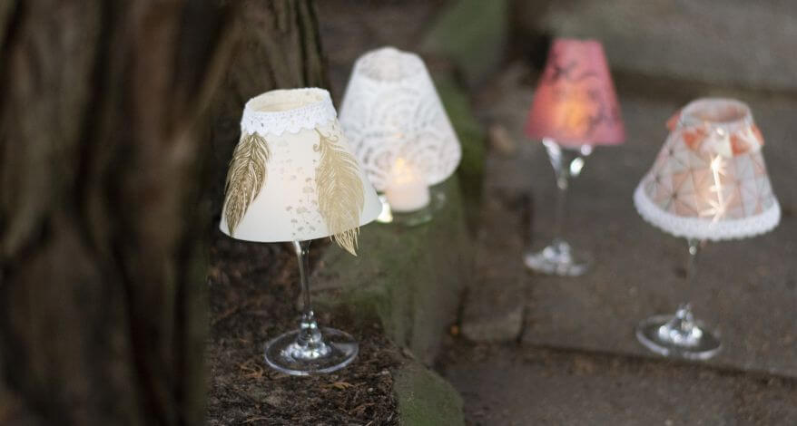 Mehrere Weingläser mit bunten selbstgebastelten Lampenschirmen