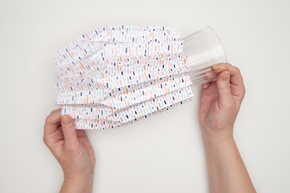 Pappvase: Jemand schiebt ein Glas in eine fertig gefaltete Pappvase aus Artoz Designpapier.