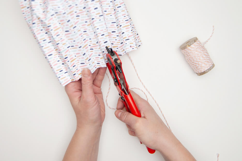 Zwei Hände stanzen mit einer Lochzange in eine fertig gebastelte Pappvase aus dem Designpapier von Artoz.