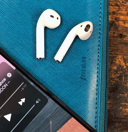 Auf einem Planer der Marke Filofax liegen zwei Kopfhörer. Am unteren Bildrand ist ein Smartphone zu erkennen, auf dem eine Musikapp läuft.