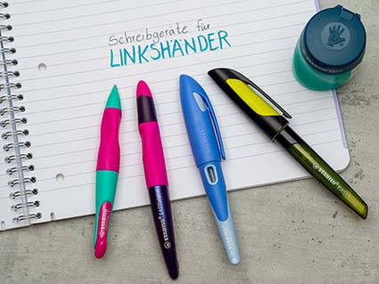 Vier unterschiedliche Linkshänder-Schreibgeräte von Stabilo liegen im Halbkreis auf einem linierten Collegeblock. Daneben steht ein Linkshänder-Spitzer. Foto: Johanna Rundel