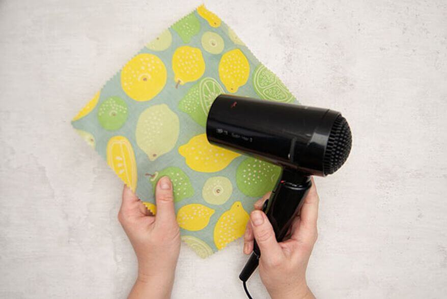 Ein quadratisches Stück gemusterter Stoff, der mit Bienenwachs (von Knorr Prandell) getränkt wurde, wird mit einem Föhn zum Glänzen gebracht. Foto: Johanna Rundel