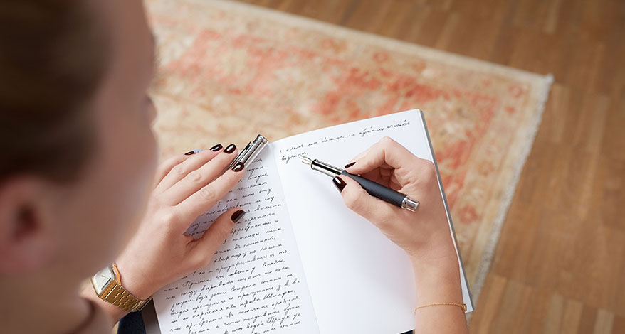 Eine Frau schreibt in eine Notizbuch einen langen Text mit einem Füller der Marke Otto Hutt.