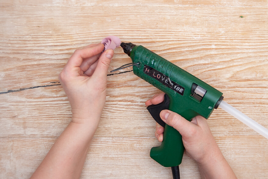 Auf einer hellen Holzoberfläche klebt jemand eine aufgewickelte Rolle rosafarbenen Tonpapier von Artoz zu einer Blume (Ranunkel) mit Heißkleber zusammen. Foto: Johanna Rundel