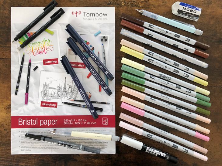 Auf einem braunen Holztisch liegen viele Zeichenmaterialien der Marke Tombow. Ein Zeichenblock, Bleistifte, Radiergummi, Fineliner und Marker. All das braucht man zum Zeichnen von Manga. Foto: Reyhan Yildirim