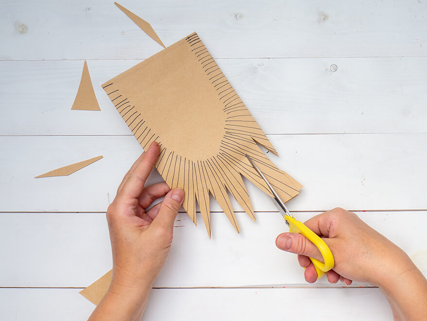 Jemand schneidet aus dem oberen Teil einer, mit schwarzen Strichen, bemalten braunen Papiertüte von Artoz Zacken aus. Der Untergrund ist weiß. Foto: Johanna Rundel
