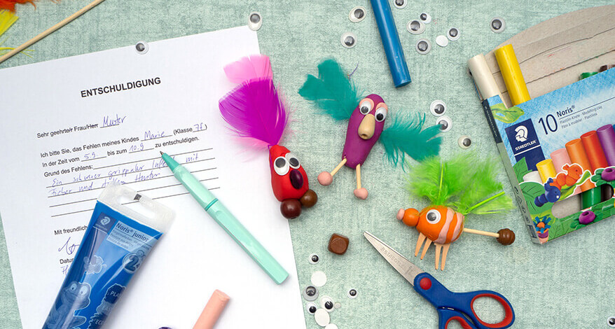 Auf einem türkisfarbenen Untergrund liegt ein ausgefüllter Ausdruck einer Entschuldigung für die Schule. Auf dem Dokument liegt ein türkisfarbener Tintenroller und eine selbstgebastelte Figur aus lila Knete von Staedtler, Wackelaugen, Perlen und Federn. Drumherum sind weitere Figuren verteilt, sowie das dazu benötigte Bastelmaterial. Foto: Johanna Rundel