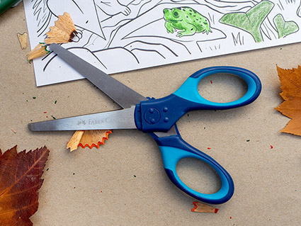 Auf einem Kraftpapier liegt eine aufgeklappte, blaue Schere der Marke Faber-Castell. Drumherum sind Herbstblätter, Bleistiftspitzer-Reste und ein Ausmalbild zu sehen. Foto: Johanna Rundel