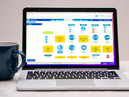 Auf einer hellen Oberfläche vor einer hellen Wand steht ein aufgeklappter silberner Laptop. Auf dem Bildschirm ist die Freeware Design & Print von Avery-Zweckform zu sehen. Links neben dem Laptop steht eine blaue Kaffeetasse. Foto: Johanna Rundel